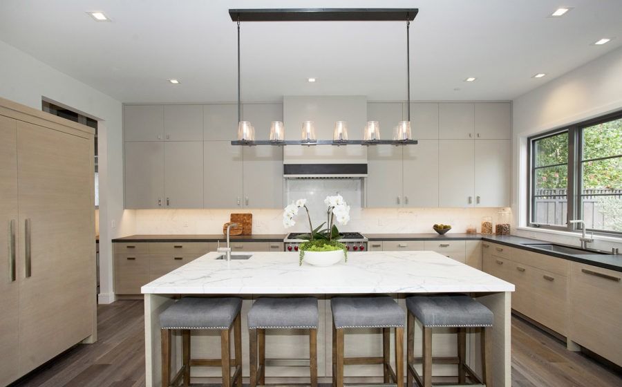 Modern kitchen with a large island, pendant lights, light gray cabinets, and wood flooring