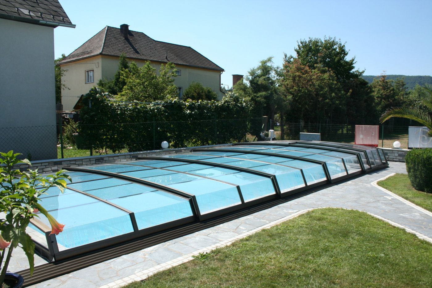 En swimmingpool med overdækning i en baggård med et hus i baggrunden.
