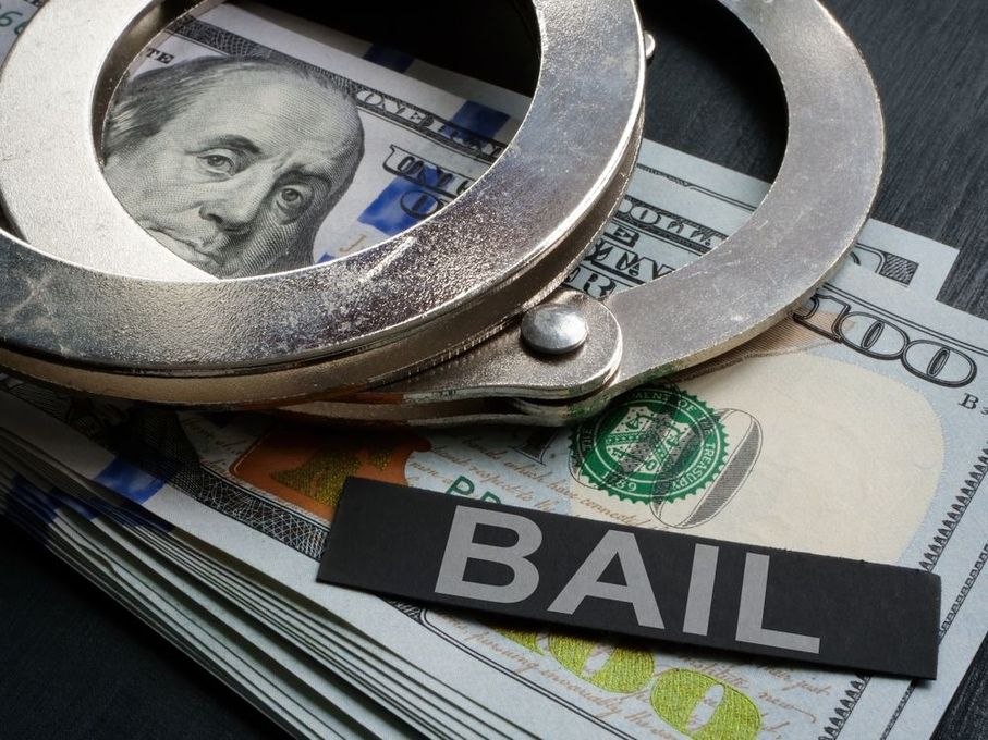 Handcuffs resting on a stack of hundred-dollar bills with a black sign labeled 