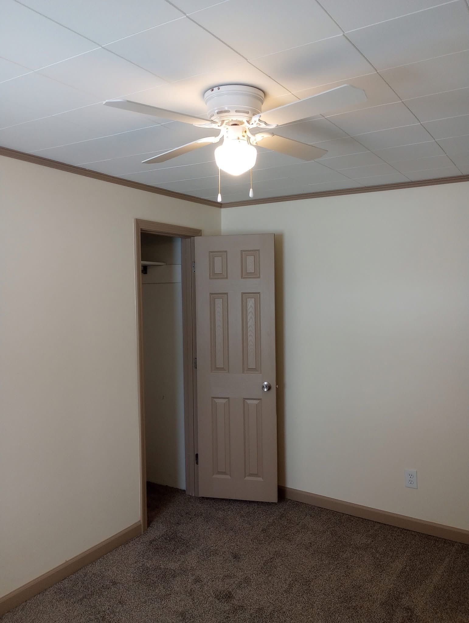 Empty beige bedroom with a ceiling fan, open closet, and carpeted floor.