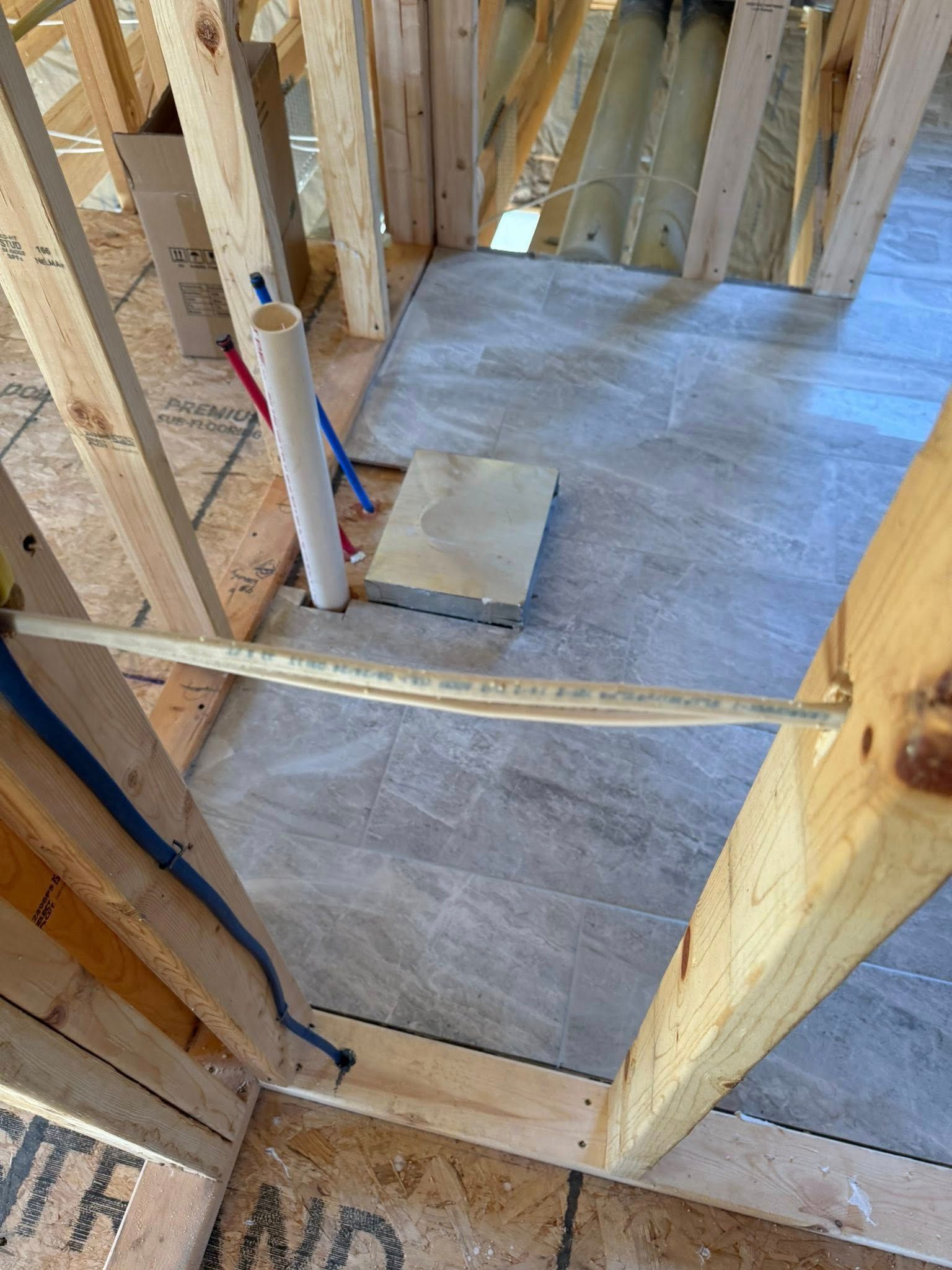 Unfinished room framing with subfloor, exposed wood studs, and plumbing pipes near a floor opening