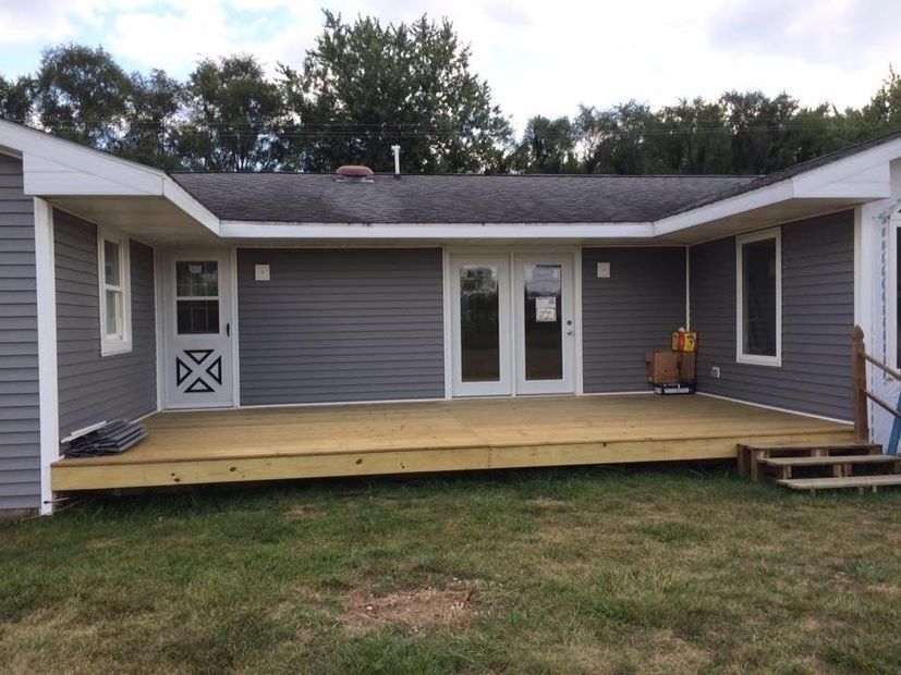 Back porch with gray siding, white doors, and a wooden deck in a grassy backyard.