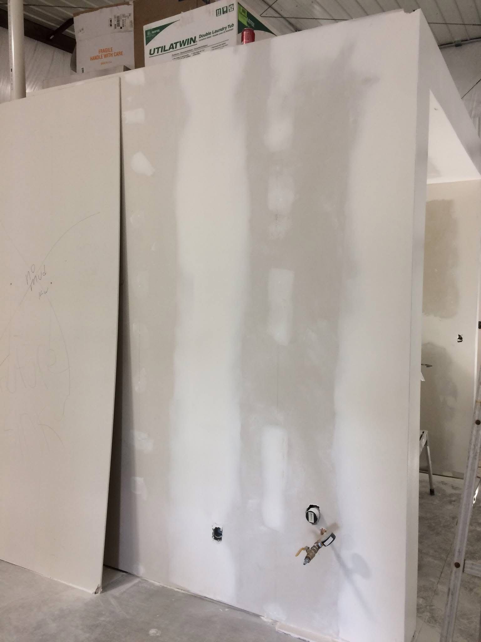 White drywall panel in a construction area, with two exposed plumbing fixtures near the bottom.