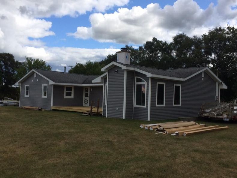Gray house with white trim and a small porch on a grassy lot under a cloudy sky