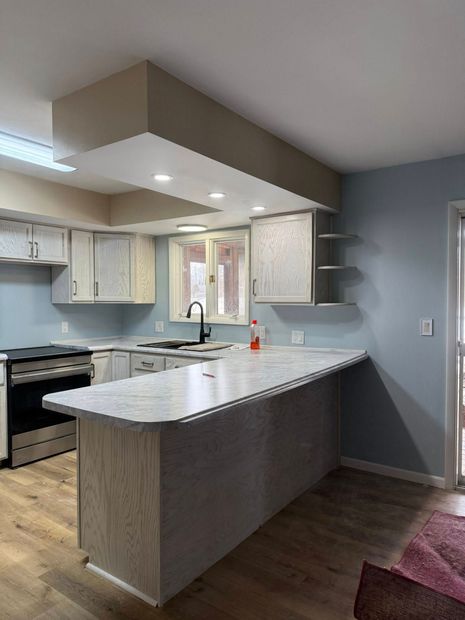 Modern kitchen with white island, beige cabinets, dark wood floor, and recessed ceiling lights
