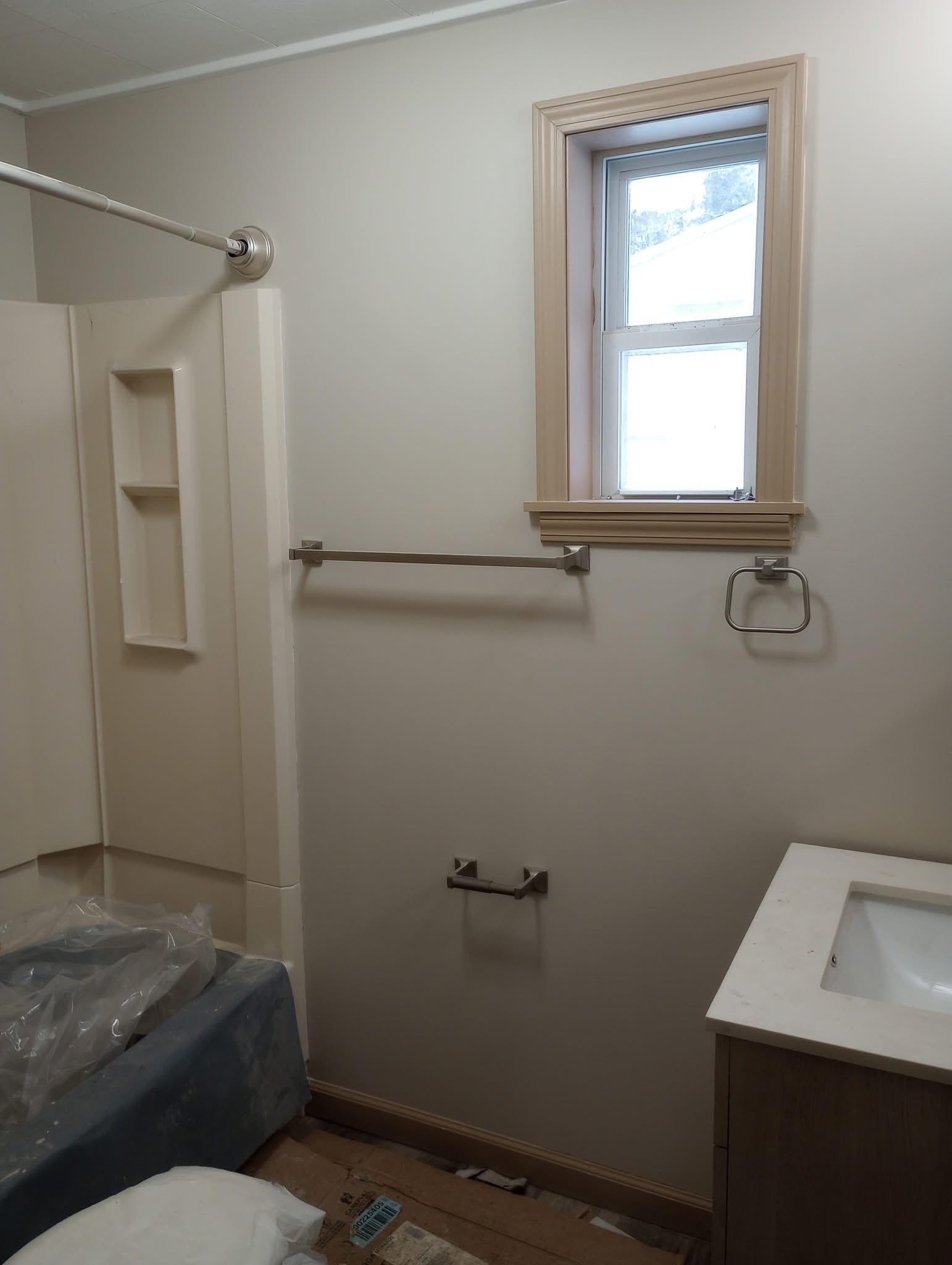 Bathroom under renovation with shower curtain rod, window, towel bars, and a vanity sink.