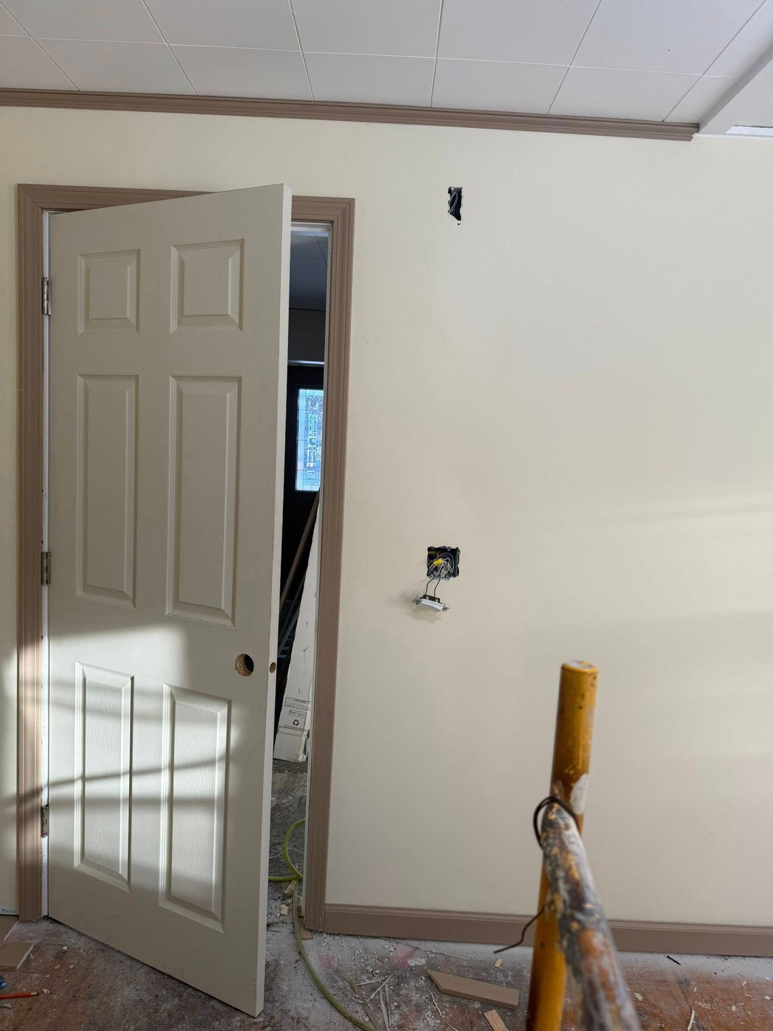 Partially painted room with white walls, open door, and a paint roller in the foreground