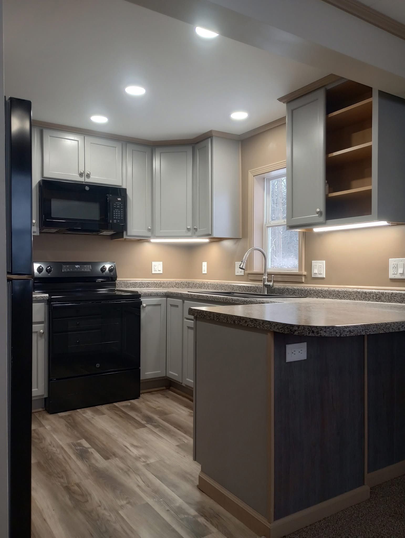 Modern kitchen with dark cabinets, black appliances, granite island, and wood-look flooring