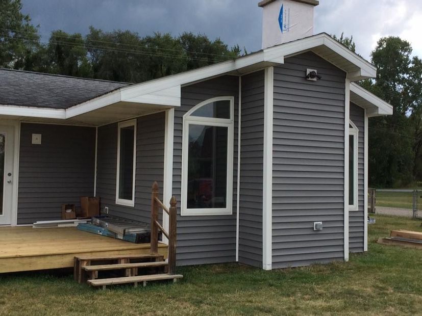 Gray house exterior with white trim, covered porch, and steps on a grassy lot