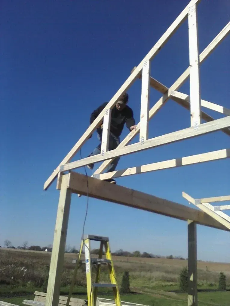 Worker on a roof frame above a yellow ladder under a clear blue sky.