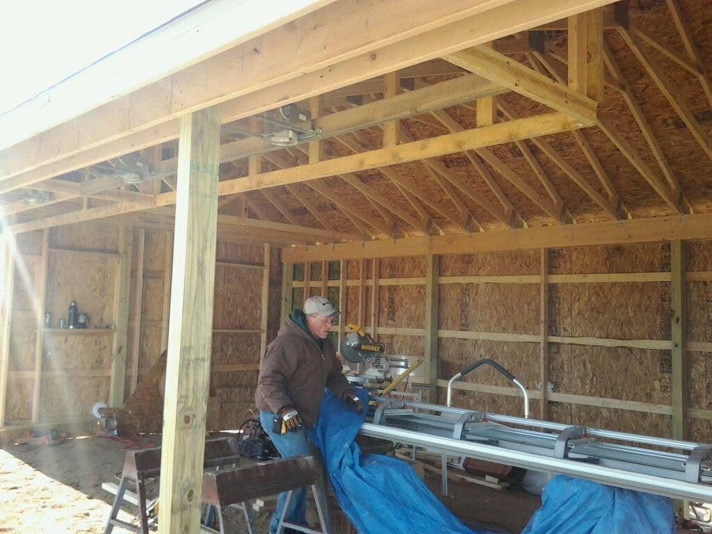Worker using a blue welding machine inside a wooden workshop with exposed framing