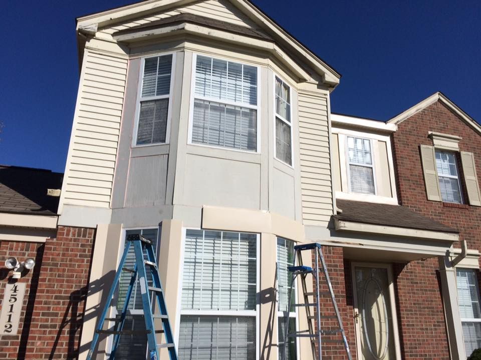 House exterior with two ladders leaning against the front facade under a clear blue sky