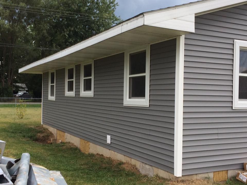 Gray house with white trim and a sloped roof, viewed from the side in a grassy yard.
