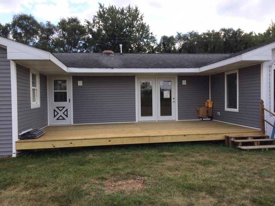 Gray house with a wide wooden accessibility ramp/deck leading to double doors and a small step on the right