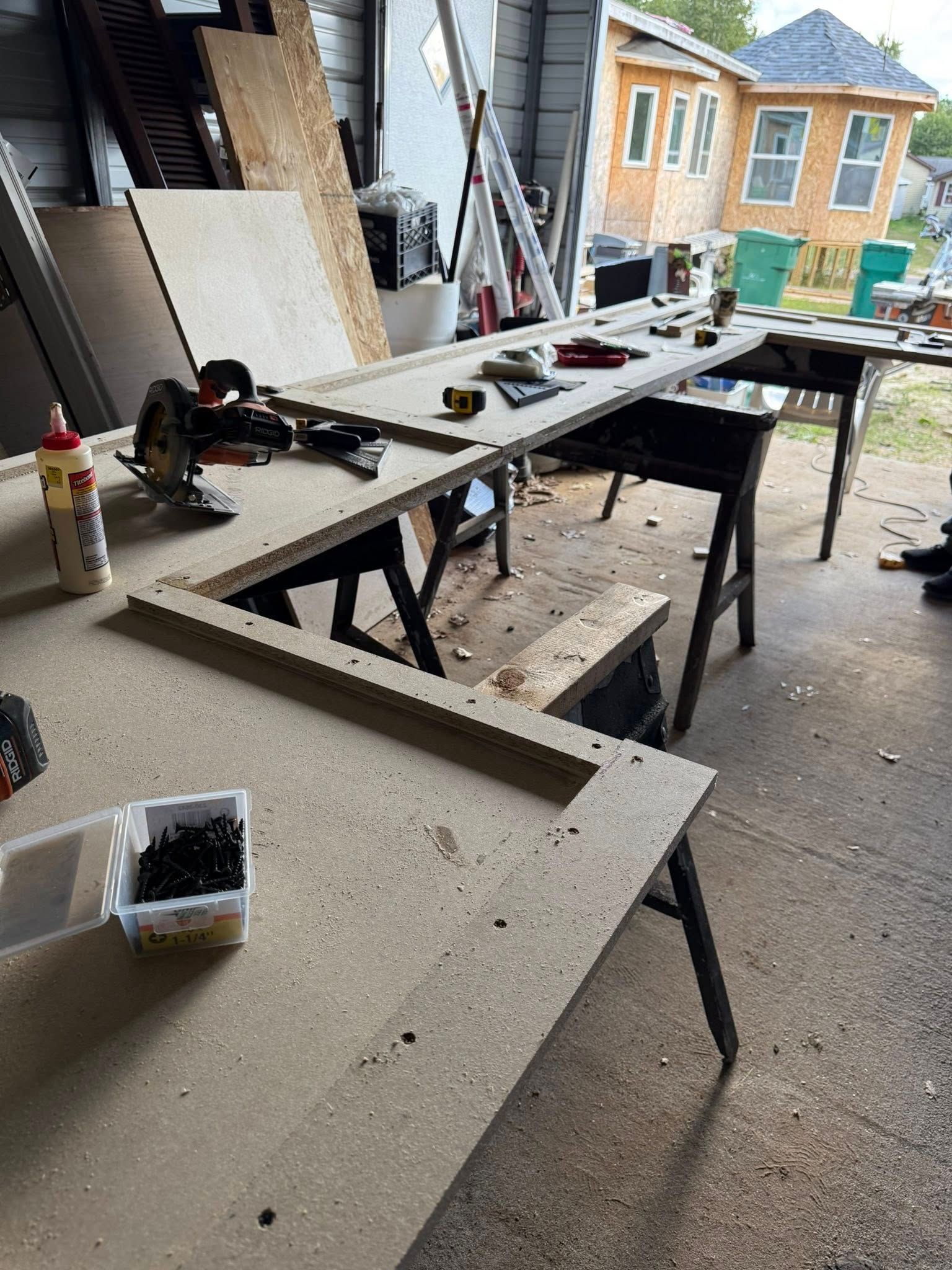 Workshop table with long wooden boards, tools, and clamps in an outdoor work area