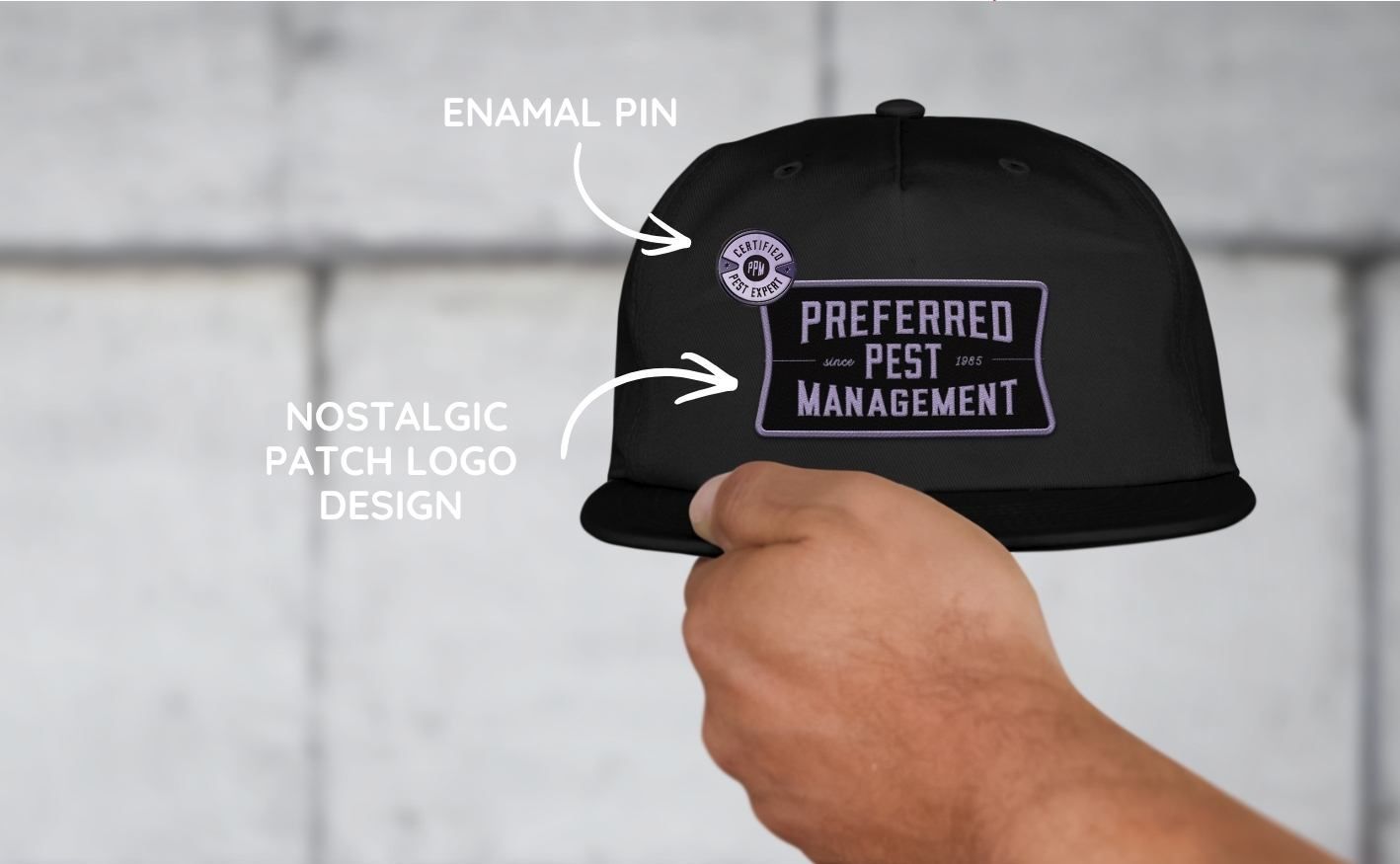 A hand holds a black baseball cap featuring a