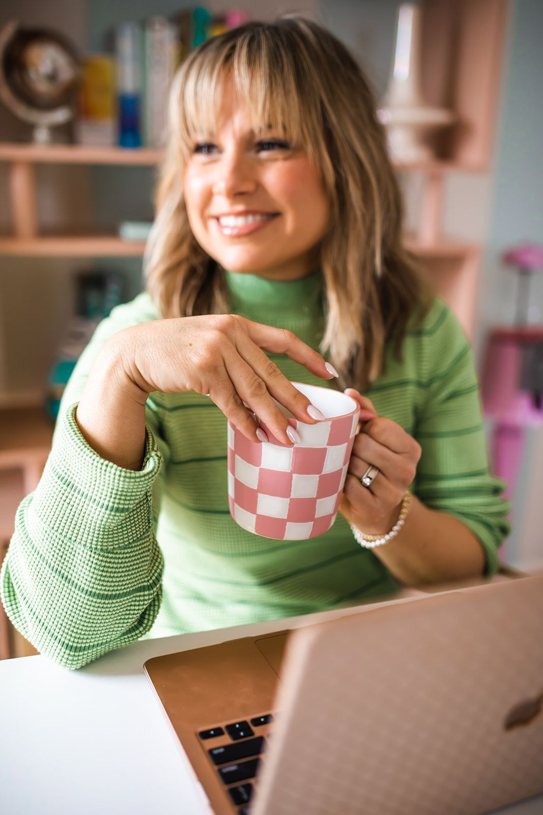 A woman is sitting at a desk with a laptop and a cup of coffee.