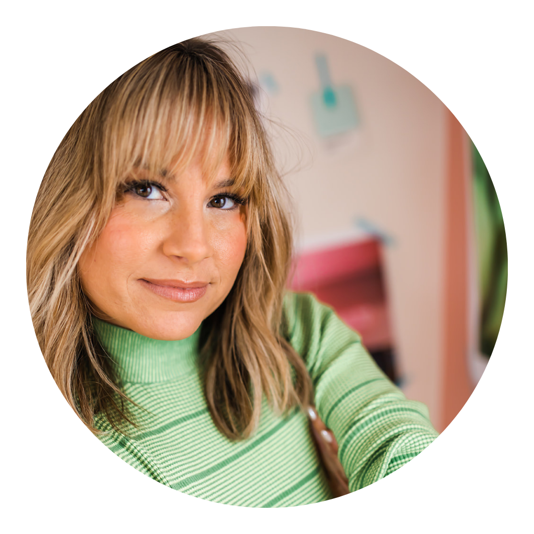 Woman with blonde hair, bangs, in a green sweater, looking at the camera. Soft focus background.