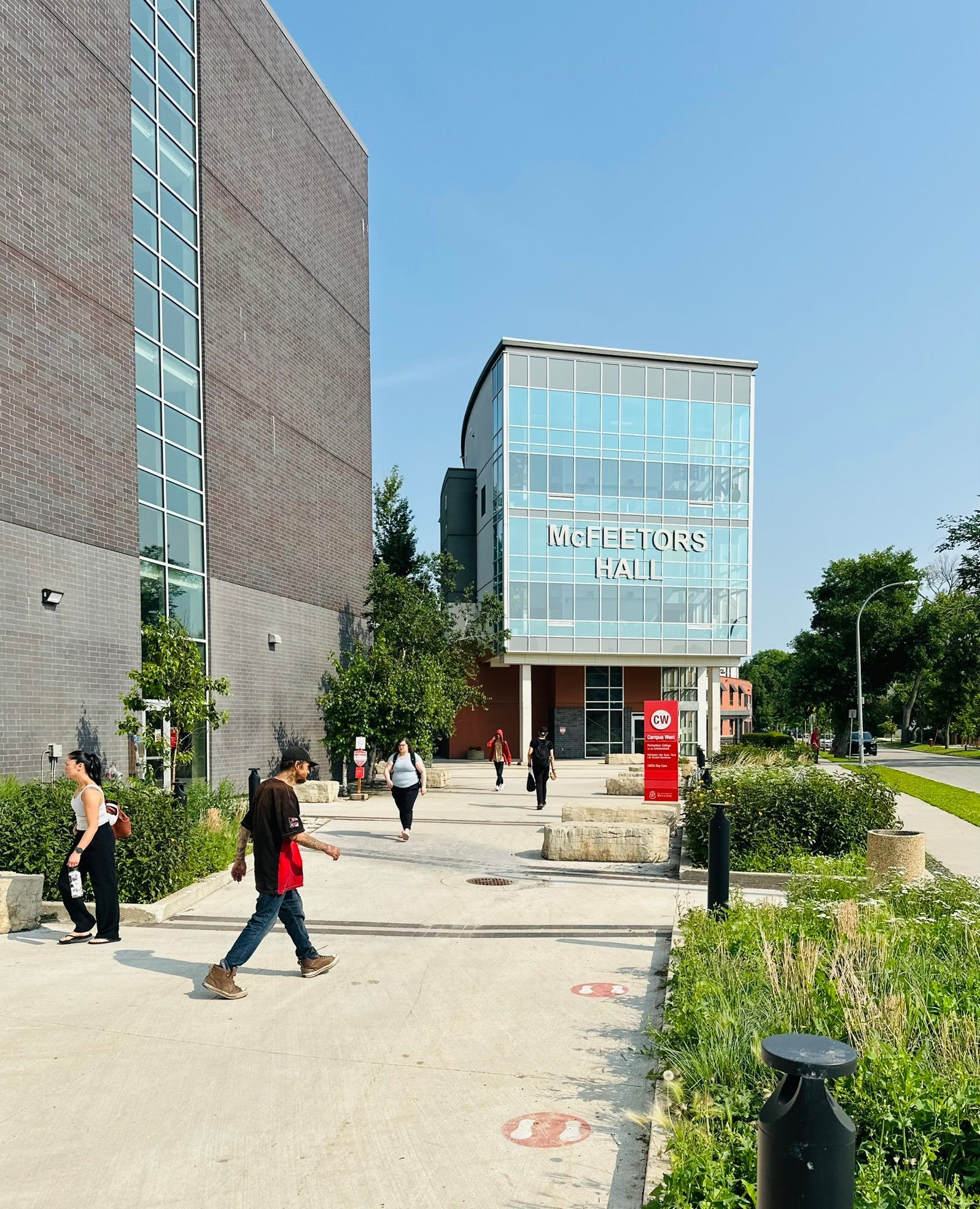 People walking on a campus path beside modern glass buildings on a sunny day.