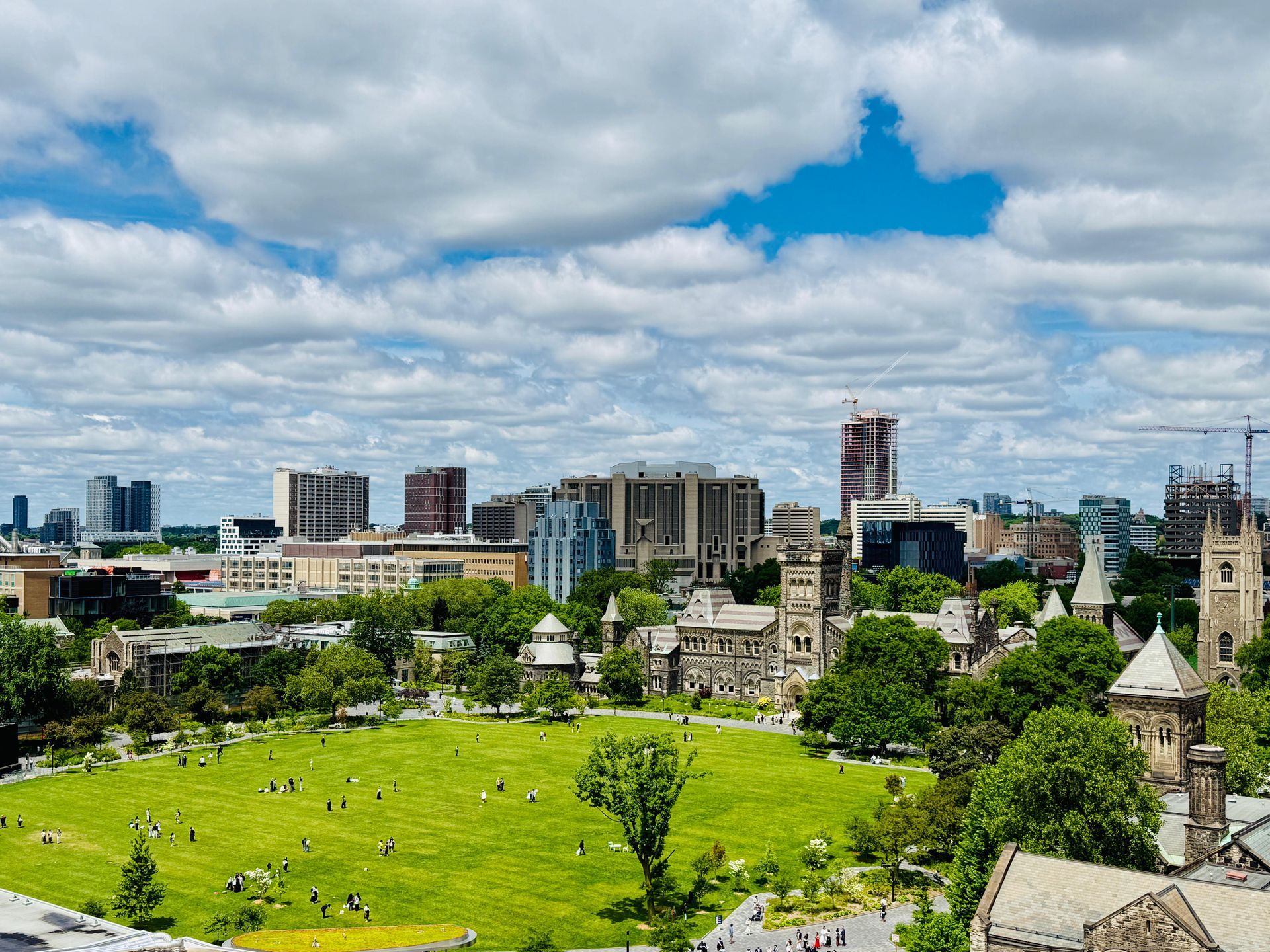 City skyline behind a bright green park under a cloudy blue sky