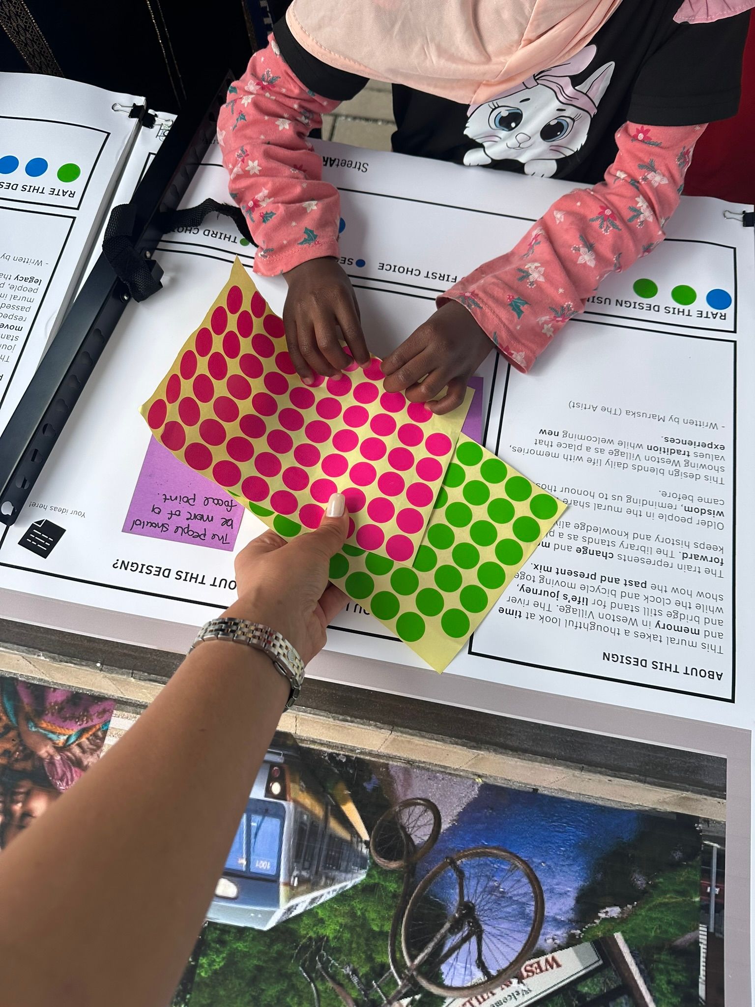 Hands place colorful dot stickers on a worksheet at a classroom table.