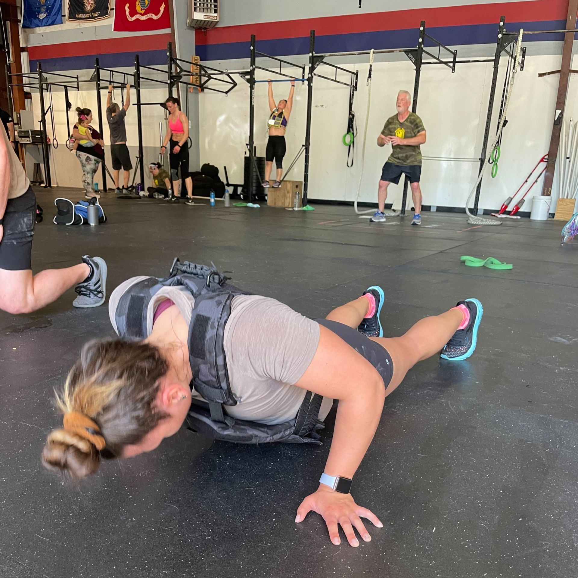 Woman doing push-ups on a gym floor with others exercising in the background at Perry Hall Fitness & Performance in White Marsh, MD