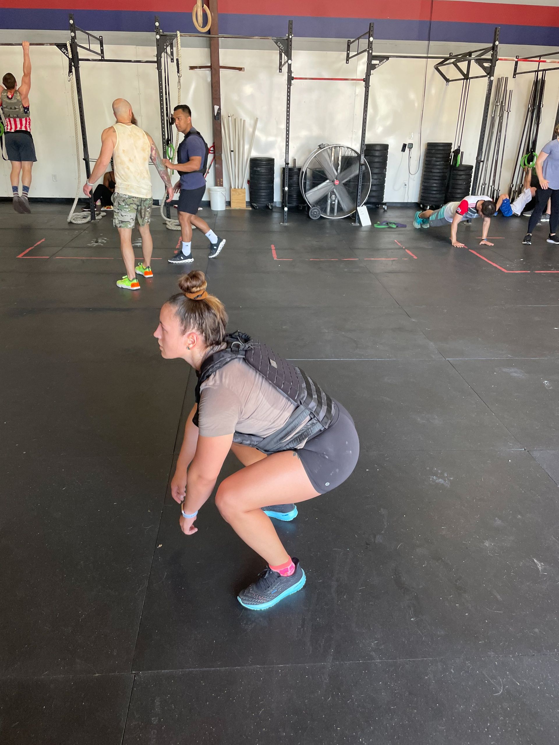 People doing squats in a gym with pull-up rigs and gym equipment in the background at Perry Hall Fitness & Performance in White Marsh, MD