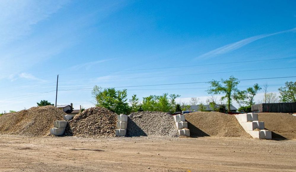 Piles of gravel and rock with concrete retaining blocks, under a blue sky.