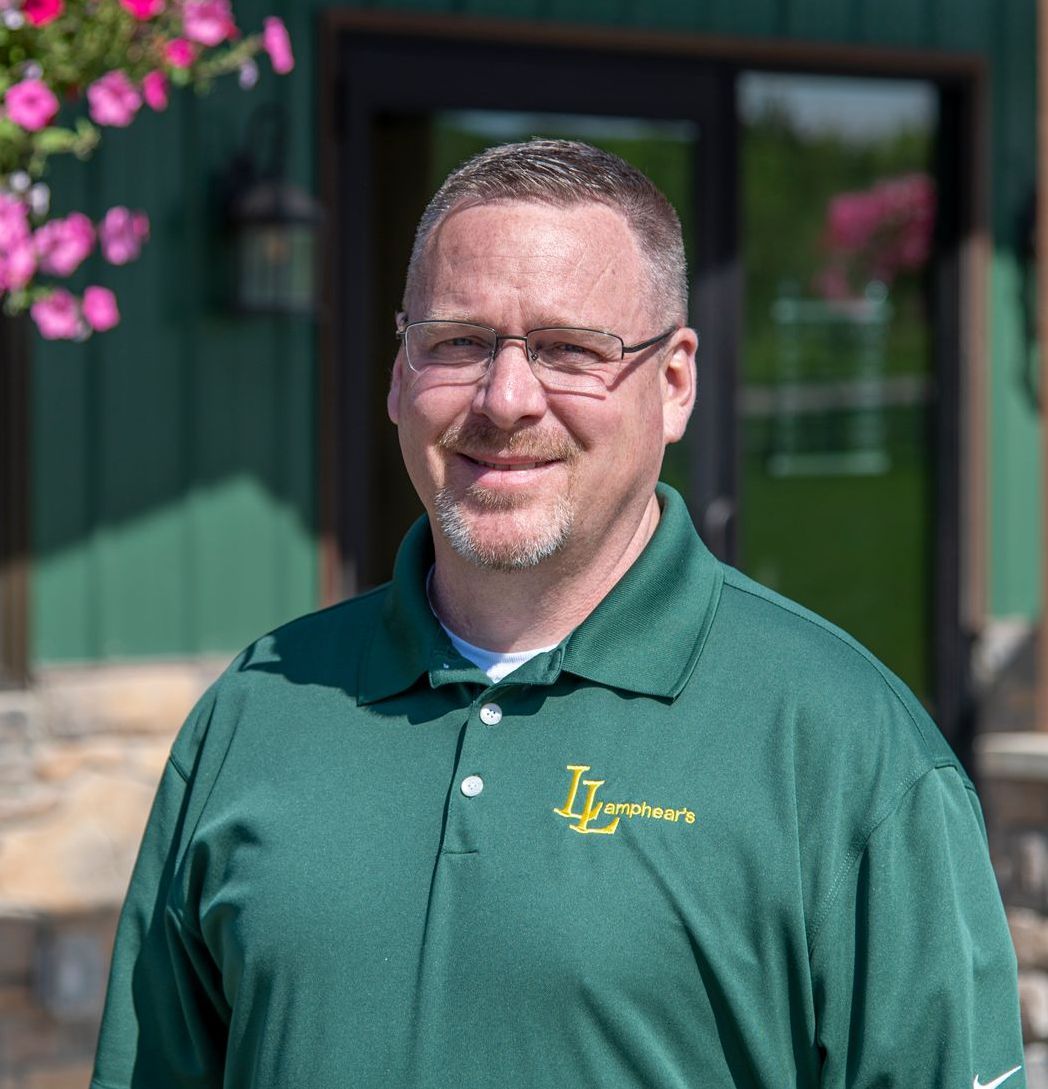 Man in green polo shirt smiles, standing outdoors in front of a green building.