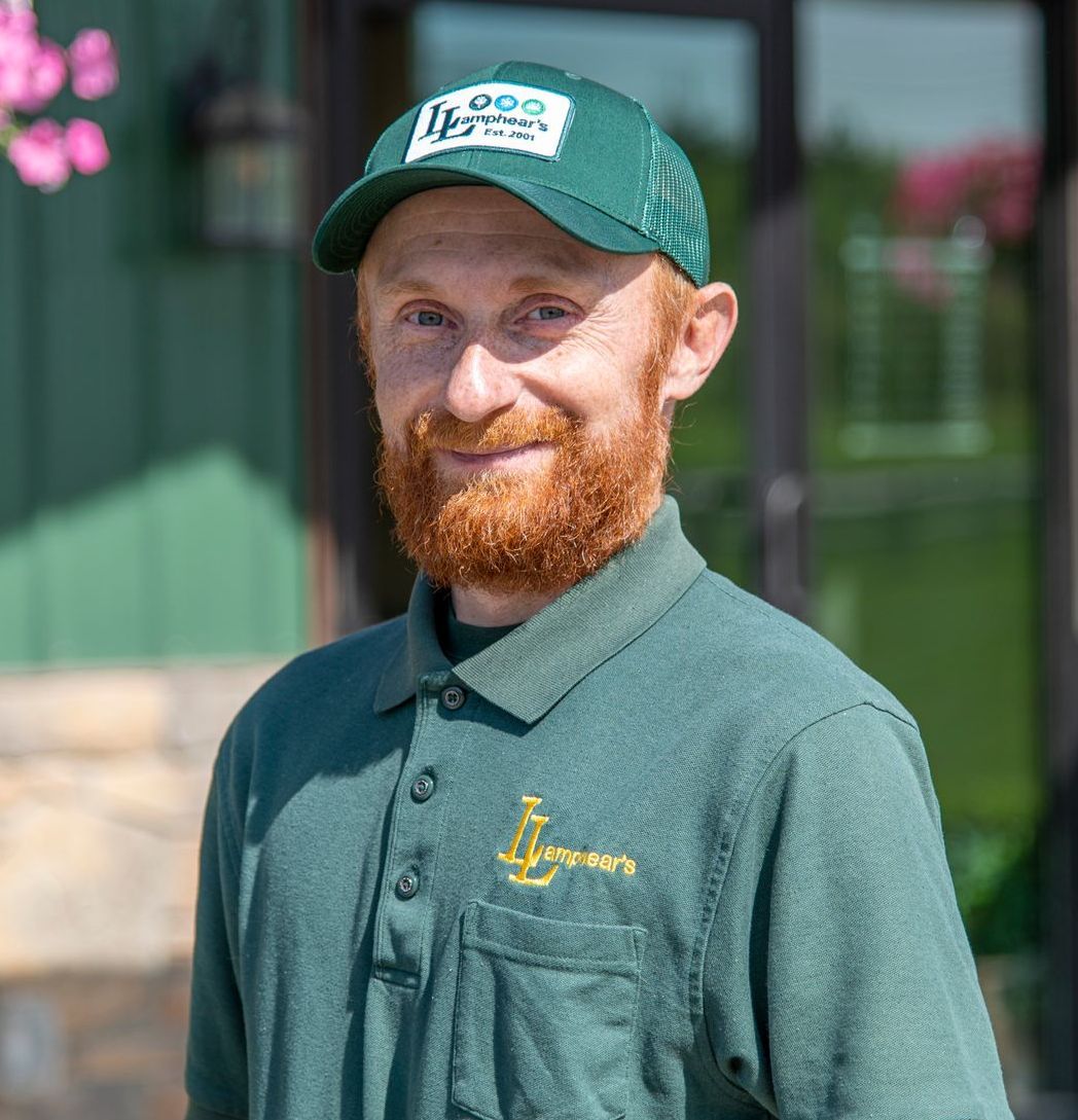 Man with red beard wearing a green hat and shirt, smiling outdoors.