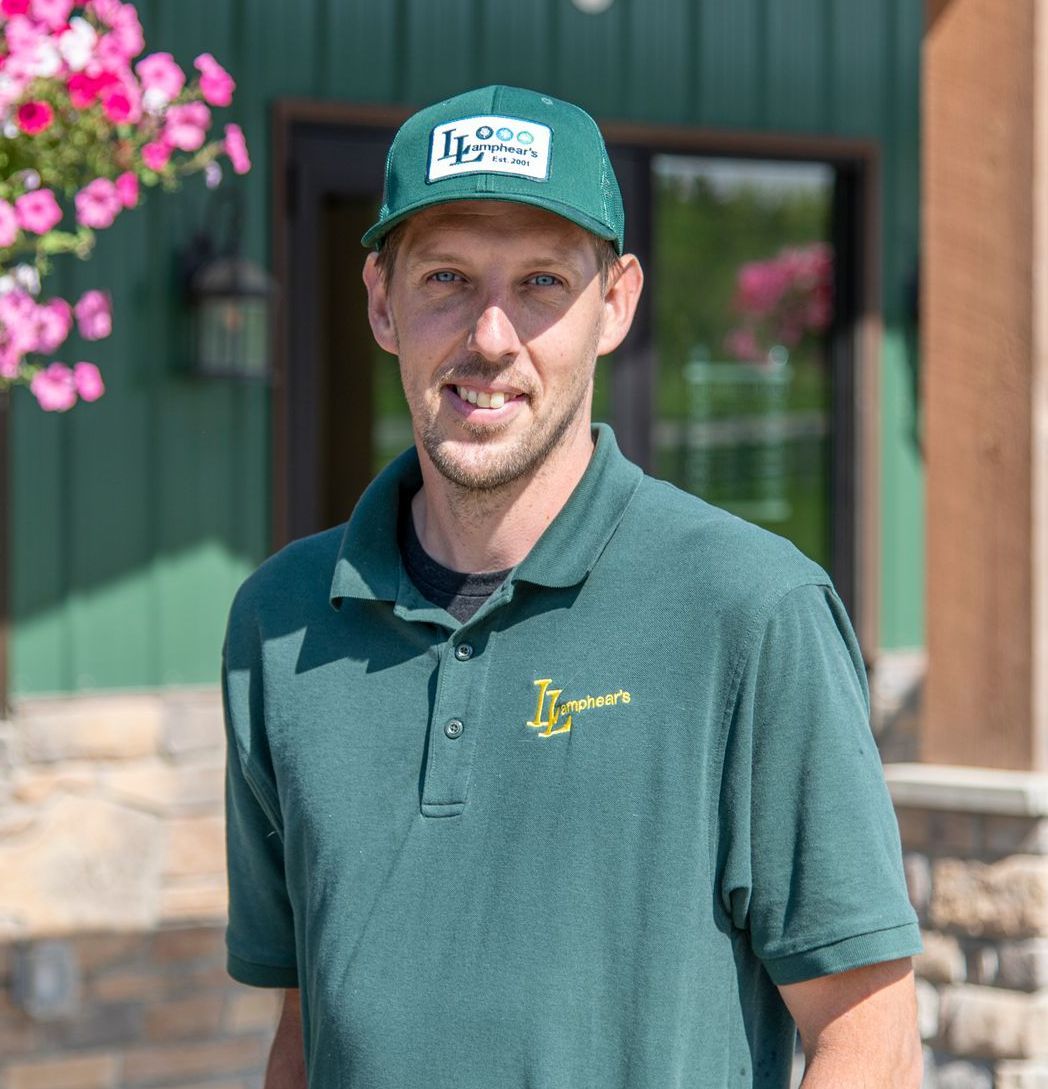 Man in green polo and cap, smiling, standing outside a building with flowers.