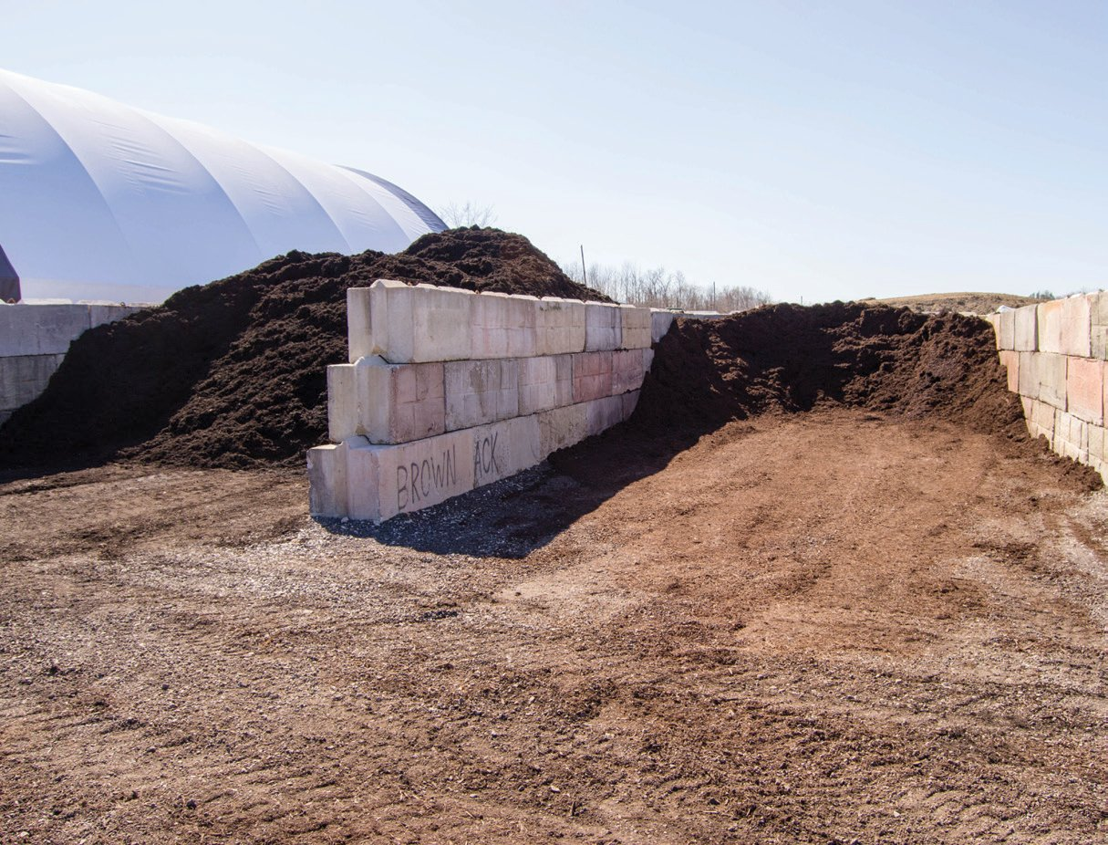 Piles of mulch, varying in color, next to a concrete block wall and a large white dome.