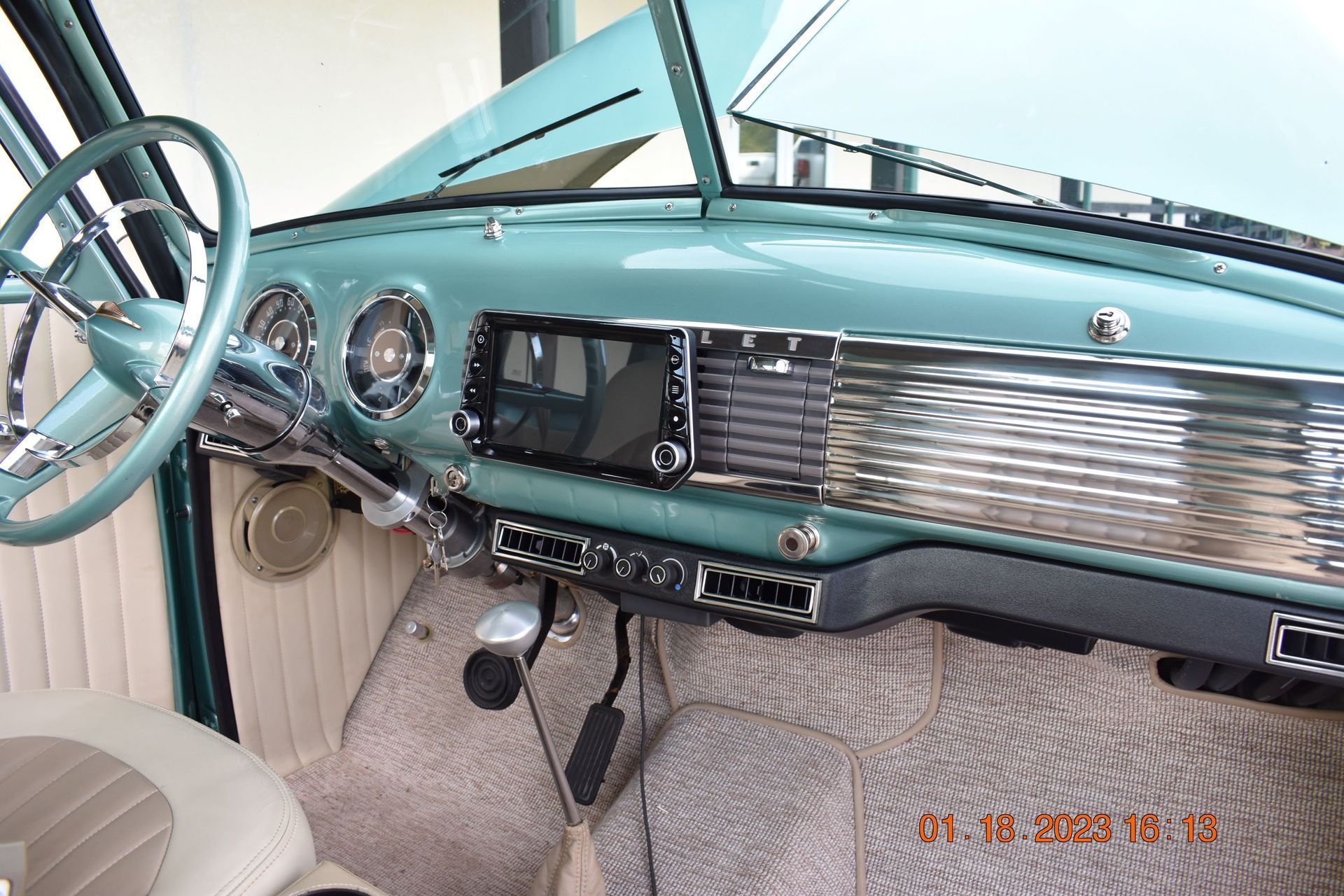 Vintage car dashboard and steering wheel in a teal and beige interior, viewed from the driver’s seat