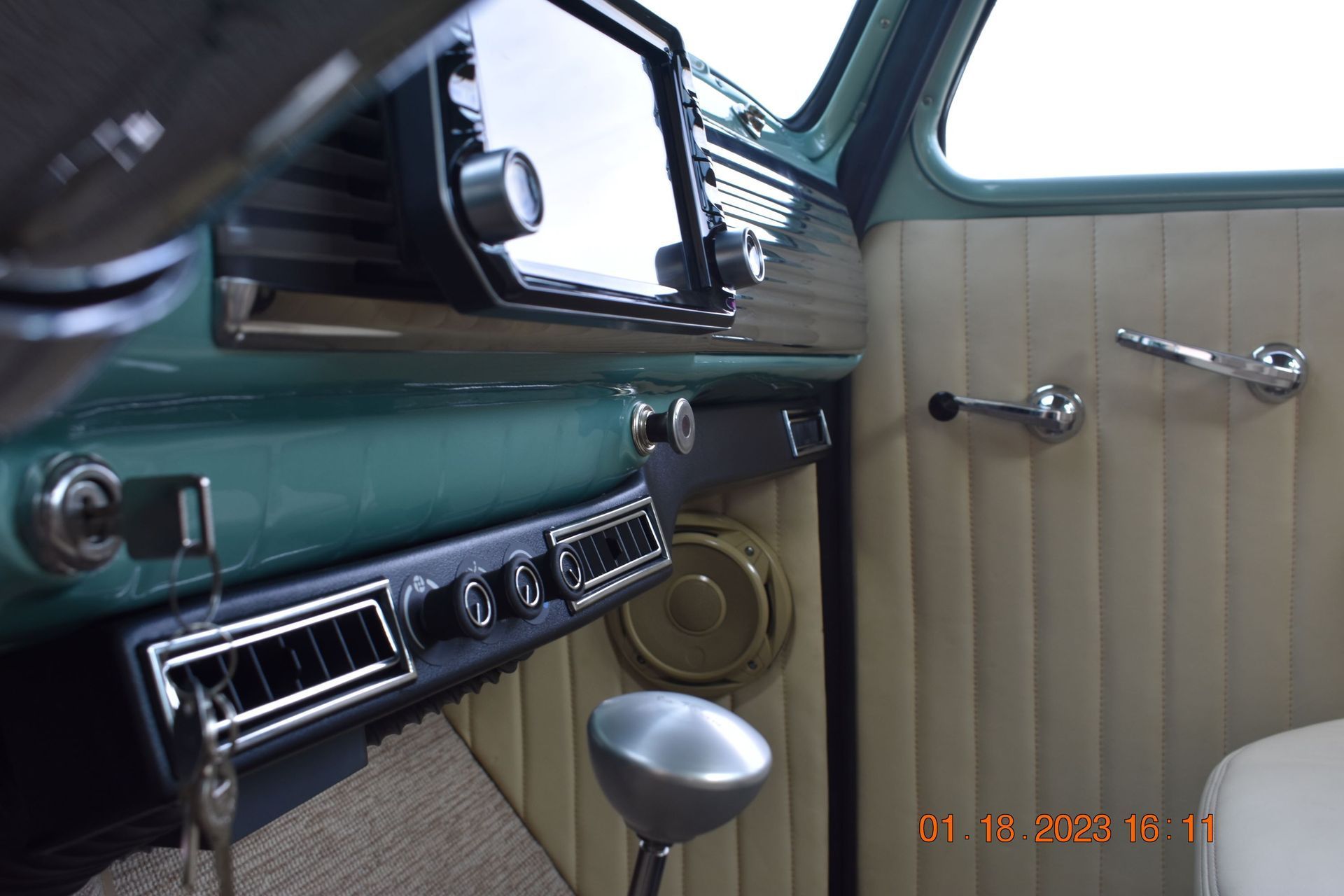 Vintage car interior with teal dashboard, chrome controls, and cream pleated door panel.