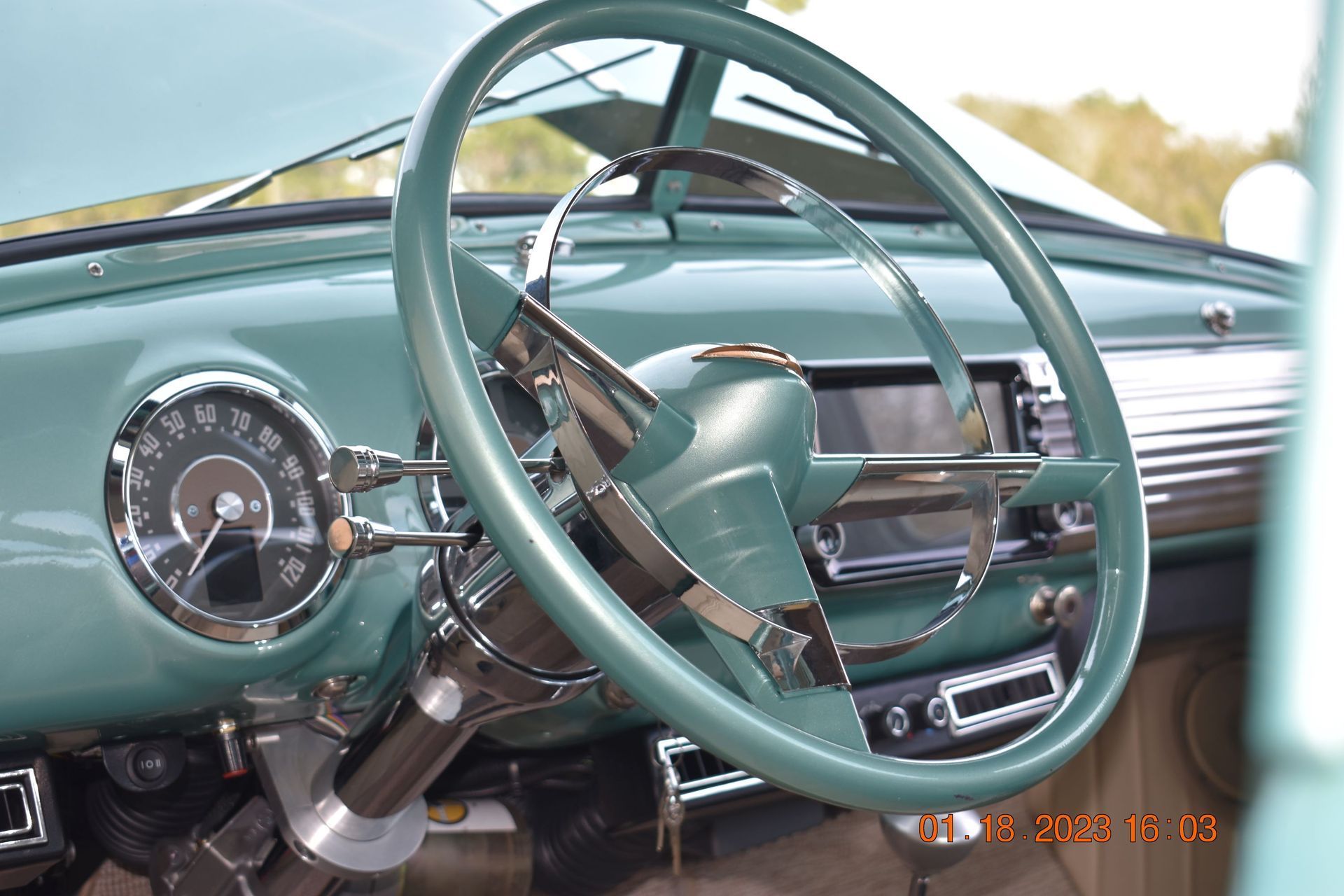 Vintage teal car dashboard with steering wheel and classic gauges, seen from the driver’s seat