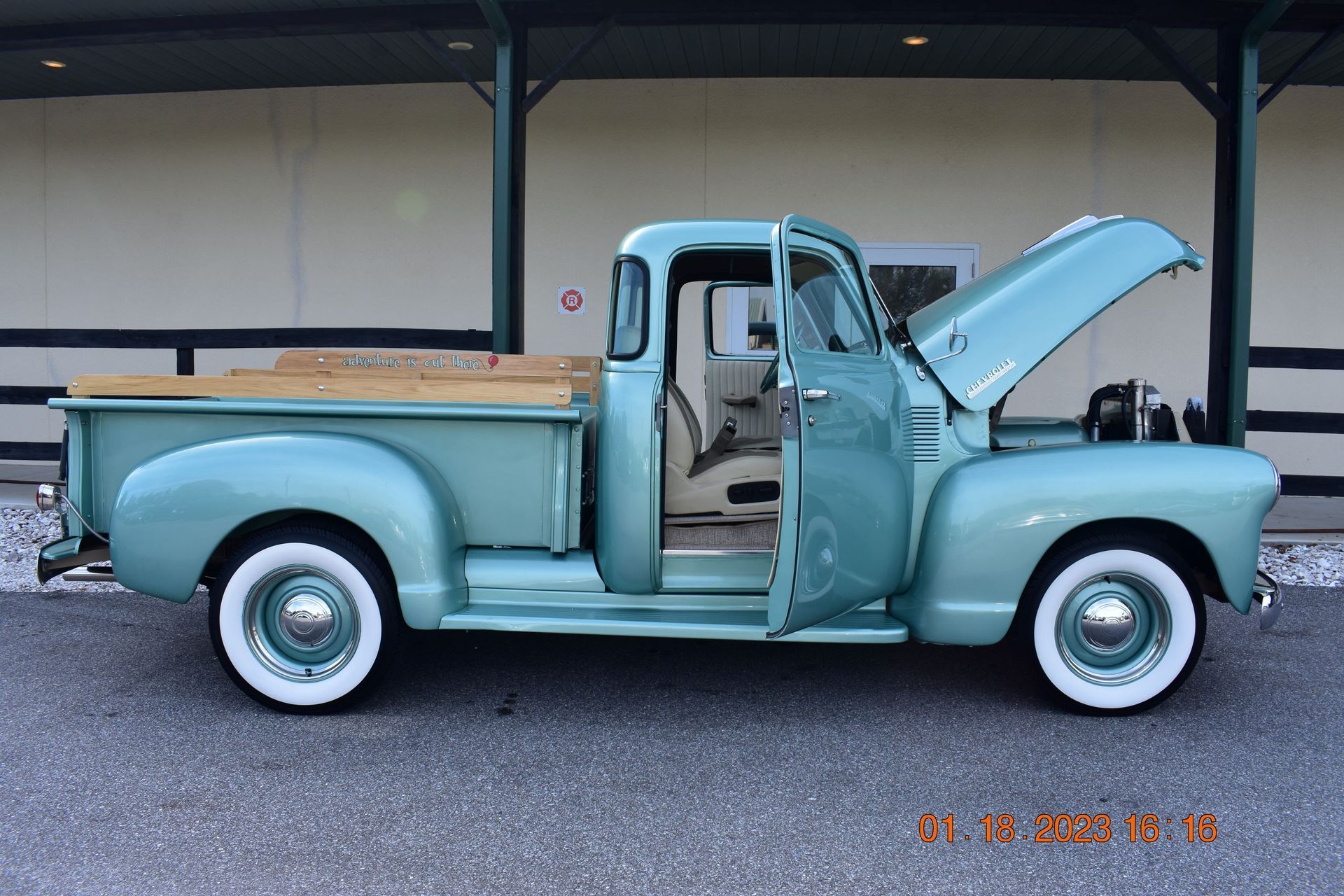 Vintage light blue pickup truck with hood open and door ajar, parked in front of a building.
