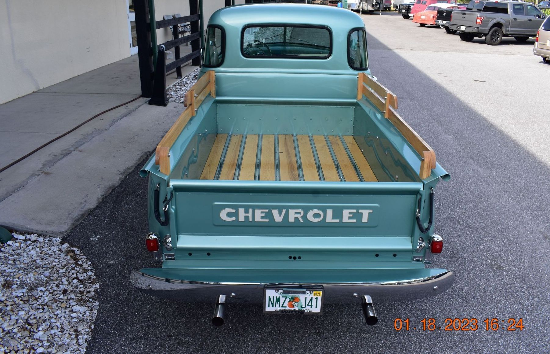 Turquoise Chevrolet vintage pickup truck parked on a street, rear view with wooden bed rails.