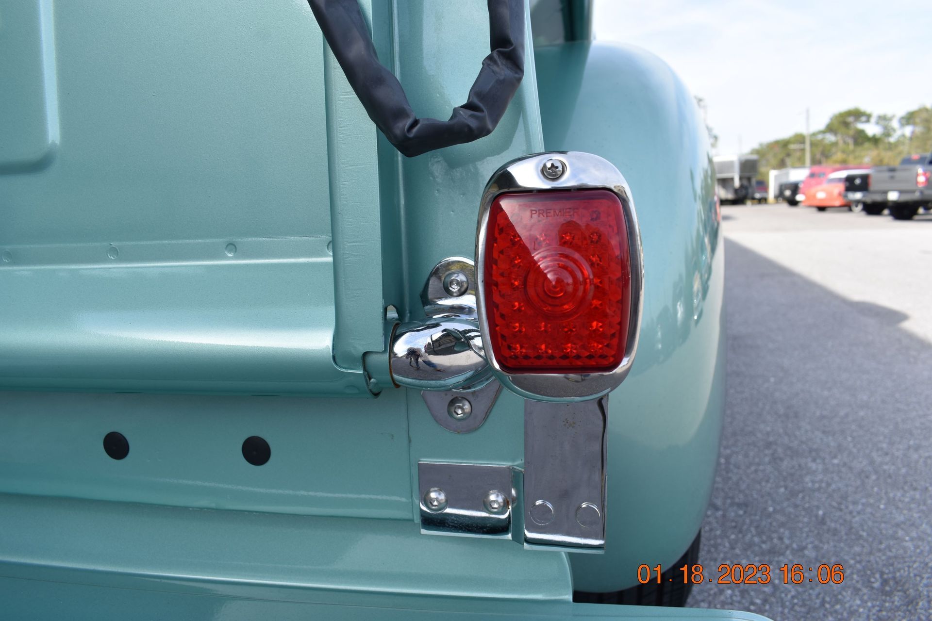 Close-up of a vintage turquoise van’s red tail light and chrome trim at a roadside parking lot.