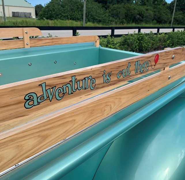 Turquoise wooden bench with “adventure is out there!” text outdoors.
