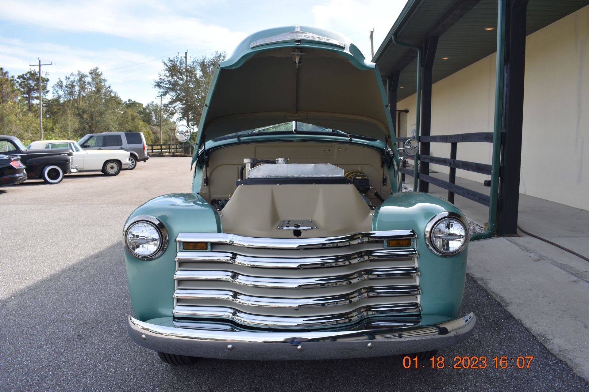 Vintage teal pickup truck with hood open outside a building