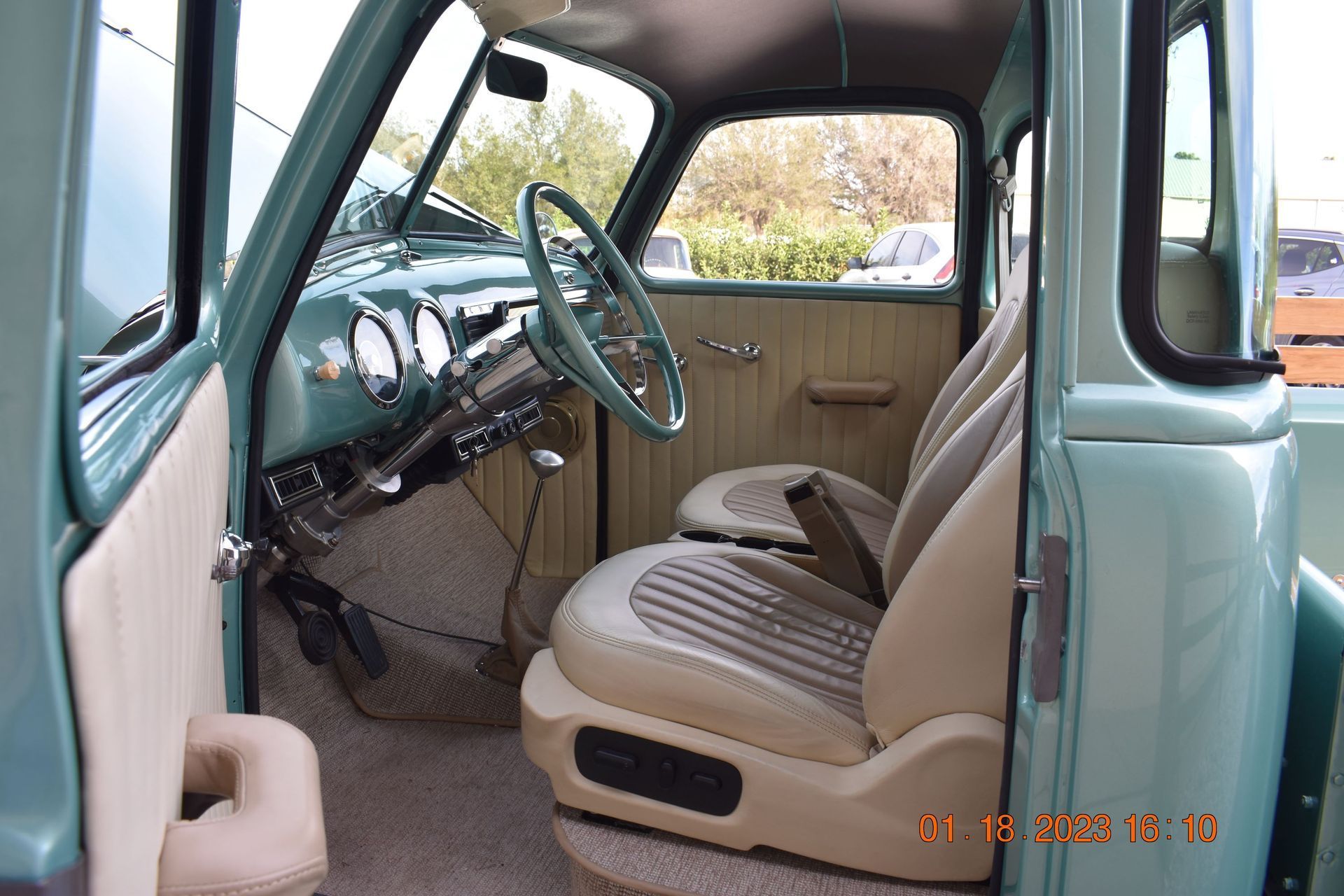 Vintage car interior with teal seats, steering wheel, and beige door panel viewed from the open door