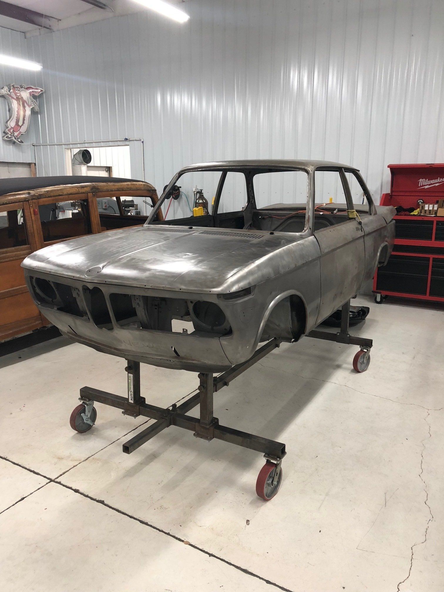 Grey classic car body shell on a wheeled stand in a workshop garage