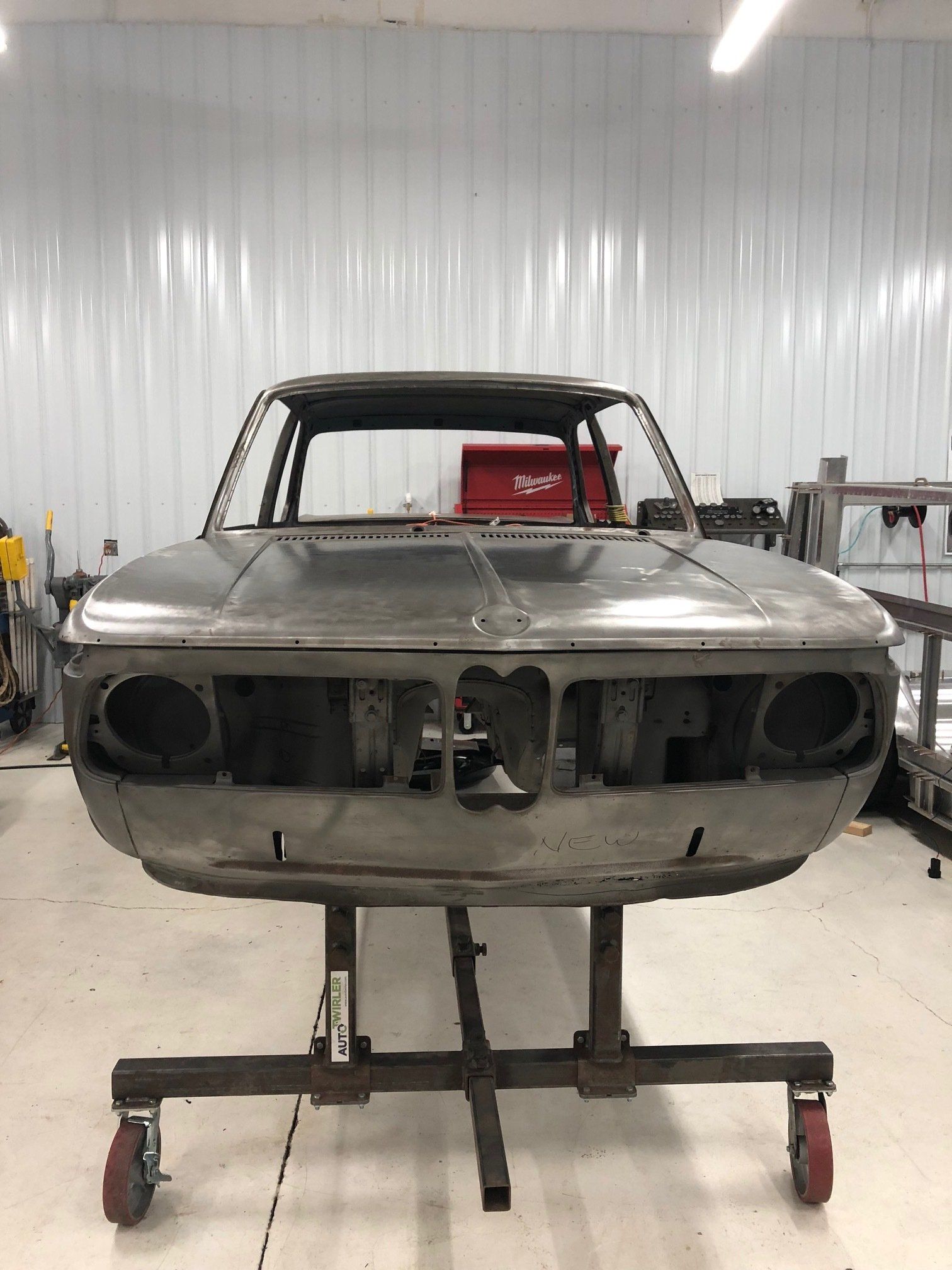 Front view of a stripped classic car body on a stand in a workshop.