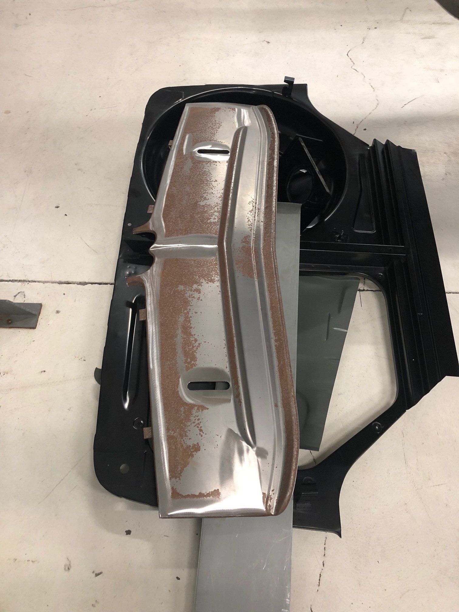 Damaged silver car bumper or trim panel lying on a floor with black frame pieces