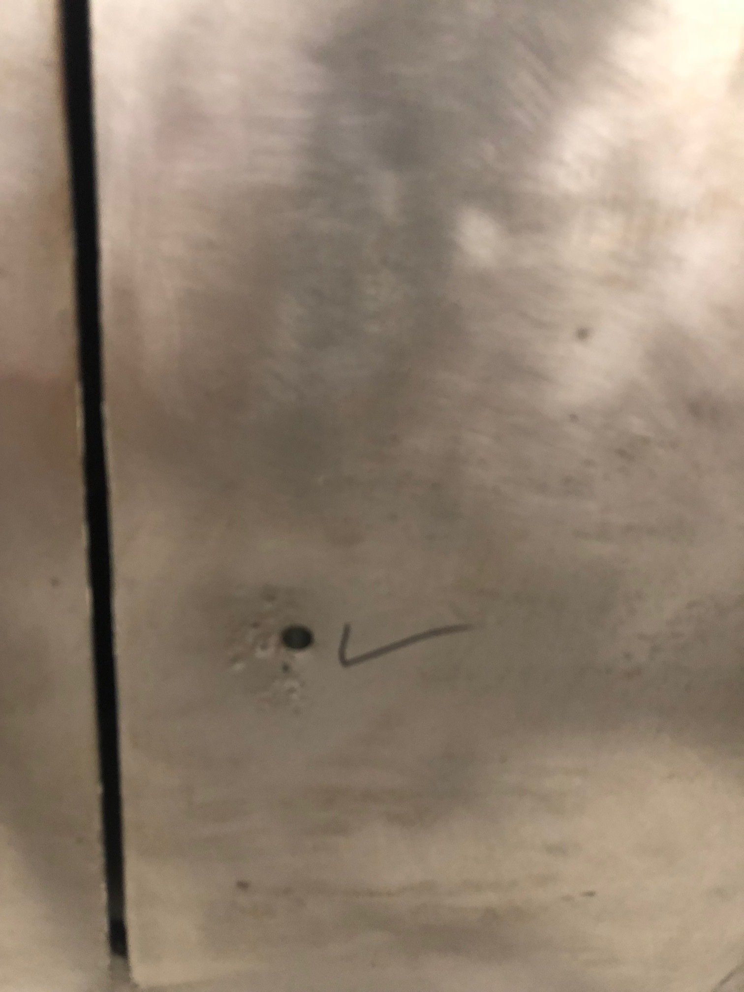 Close-up of a brushed metal surface with a small hole and a black check mark near the bottom.