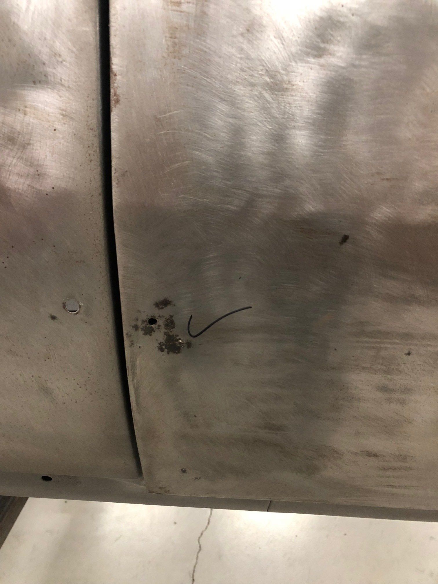 Close-up of a scratched metal surface with a vertical seam and small dark marks.