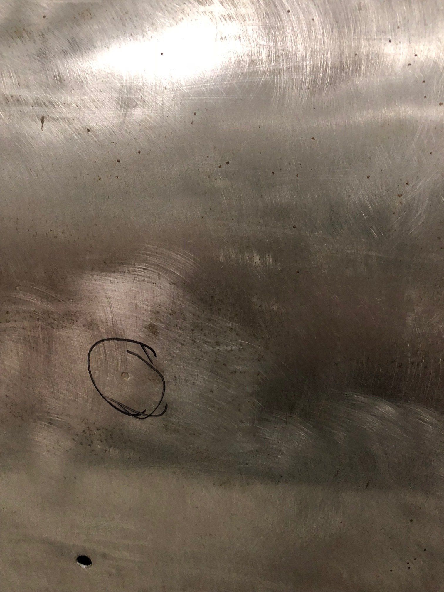 Close-up of a scratched metallic surface with a small black circled mark near the lower left.
