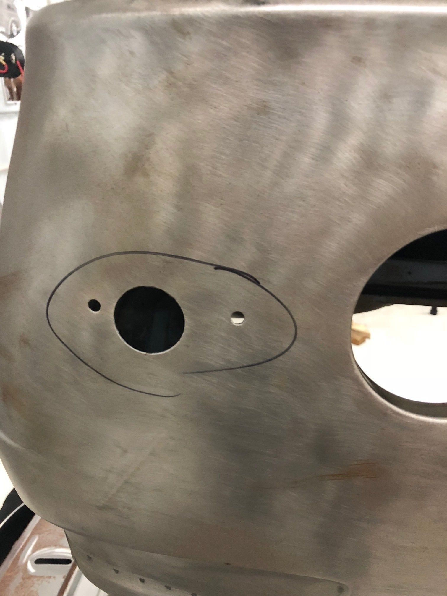 Gray metal panel with two cutout holes, one small oval outline sketched around them.