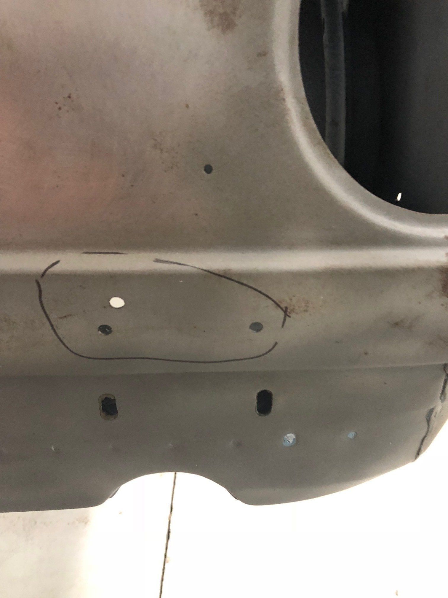 Close-up of a gray vehicle body panel with circular and rectangular cutouts, marked with a hand-drawn oval.