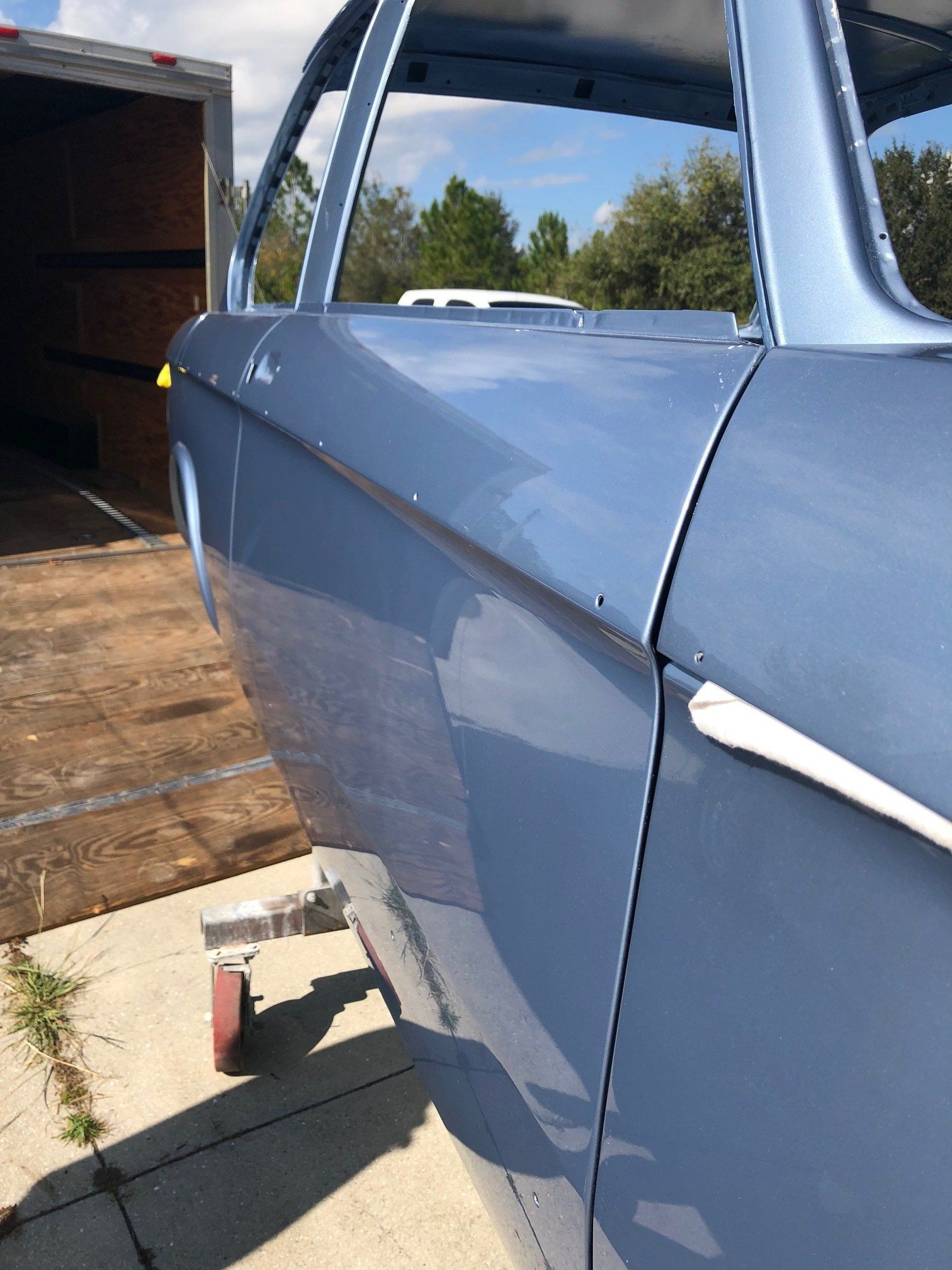 Close-up of a blue car door beside an open trailer ramp on a sunny day